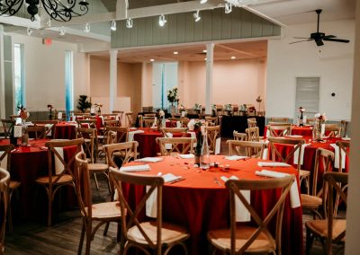 Reception room with red-linen round tables and crossback chairs set for a celebration