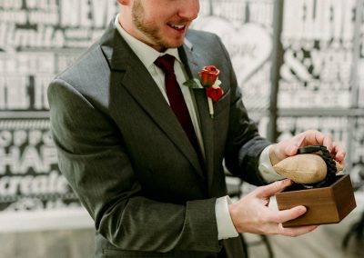 Groom opening a wooden ring box in front of a black-and-white mural wall