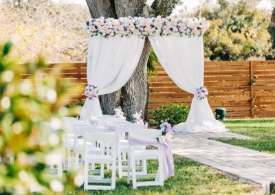 White draped ceremony arch topped with pink and white flowers over garden chairs