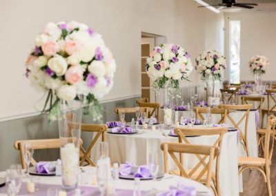 Reception tables topped with tall white and lavender floral centerpieces and purple napkins