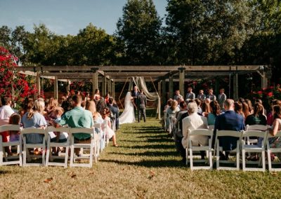 Outdoor wedding ceremony beneath a wooden pergola with seated guests