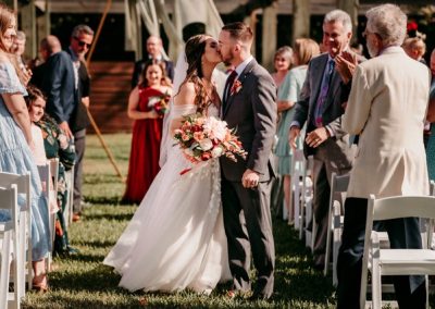 Bride and groom sharing a kiss in the aisle as guests applaud after the ceremony