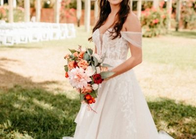 Bride holding a coral and peach bouquet on the paver path before the ceremony pergola