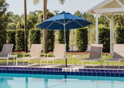 Poolside lounge chairs and a blue umbrella beside the pool with a palm tree