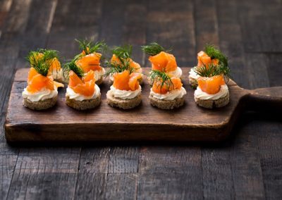 Smoked salmon and cream cheese canapes garnished with fresh dill on a rustic wooden board