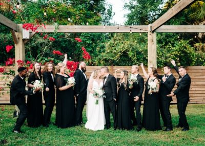 Bride and groom kissing surrounded by their wedding party in black attire outdoors