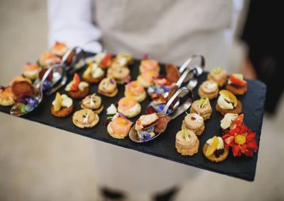 Server presenting a slate board of assorted canapes garnished with edible flowers