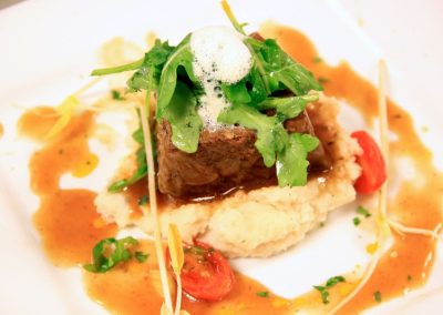 Plated beef entree over mashed potatoes with arugula and roasted tomatoes