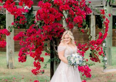 Bride holding a bouquet beneath a pergola draped in vivid red bougainvillea
