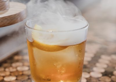 Smoking bourbon cocktail garnished with citrus on a penny-topped bar