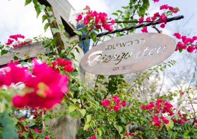 Idlewood Biergarten sign hanging amid blooming pink bougainvillea flowers