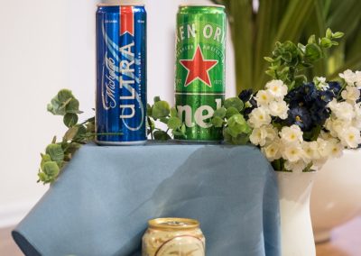 Assorted beer cans displayed with eucalyptus and white flowers on a bar table