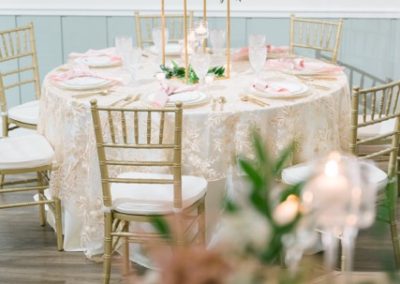 Round reception table with gold Chiavari chairs and a tall greenery centerpiece