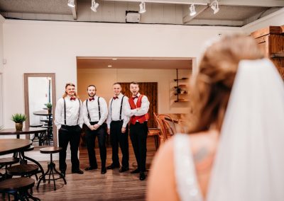 Bride watches her groomsmen react during an indoor first-look moment