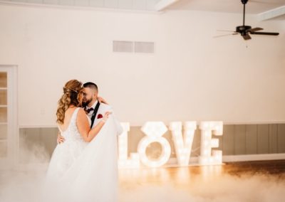 Bride and groom sharing a first dance in the fog before a lit LOVE sign