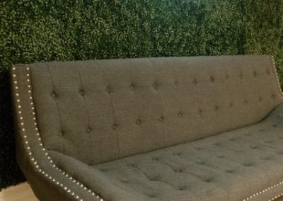 Gray tufted sofa beneath a custom The Holmes neon sign on a greenery wall