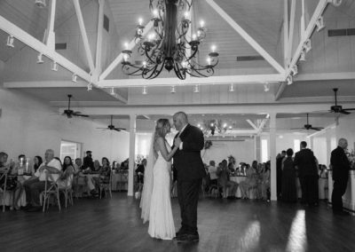 Black-and-white of a couple's first dance under the chandelier as guests look on