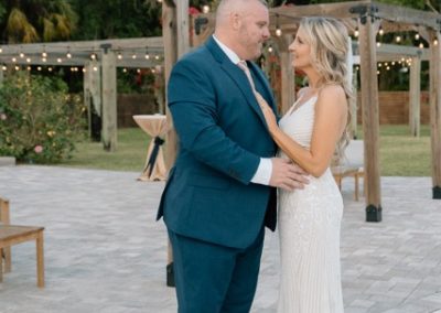 Bride and groom embracing on the patio beneath a string-lit pergola at dusk
