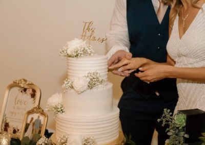 Newlyweds cutting a three-tier white cake topped with roses and baby's breath