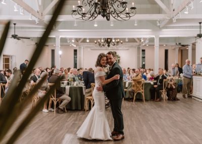 Bride and groom share their first dance under a chandelier as guests look on