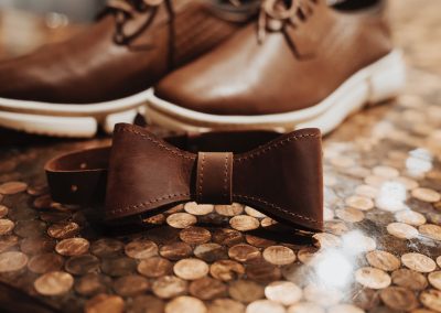 Groom leather bow tie and brown dress shoes resting on a copper penny-tiled floor