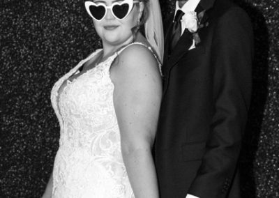 Bride in heart-shaped sunglasses and groom back to back, holding hands