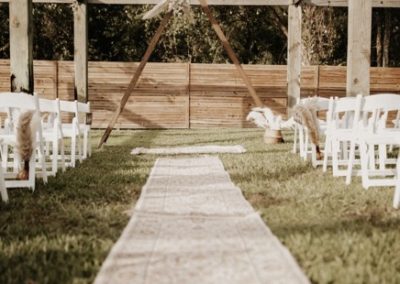 Rustic outdoor ceremony arch with a patterned aisle runner and white garden chairs