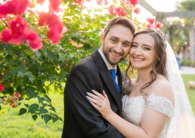 Smiling bride and groom cheek to cheek under pink bougainvillea at golden hour
