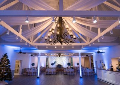Reception hall with holiday trees, blue uplighting and a draped ceiling under a chandelier
