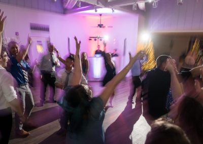 Wedding guests dancing with arms raised under purple lights on the reception floor