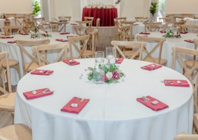 Round reception table with white linens, berry-red napkins and a floral centerpiece