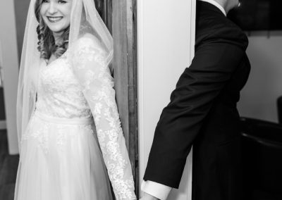 Bride and groom holding hands around a wall for a first touch, in black and white