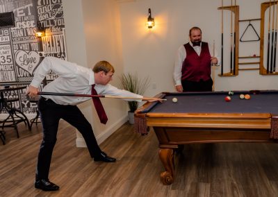 Two groomsmen playing pool in the game room with a motivational typography wall