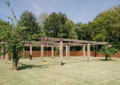 Empty outdoor ceremony space beneath a large pergola swing structure on the lawn