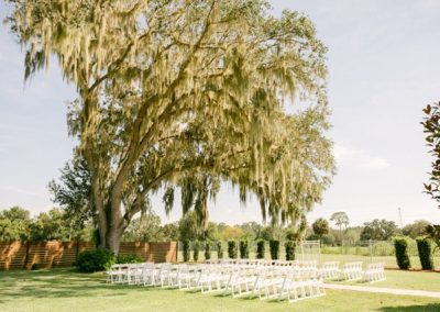 White ceremony chairs arranged on the lawn beneath a moss-draped oak