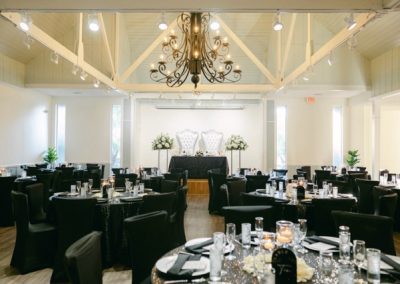 Reception hall dressed in black linens with a sweetheart table beneath an iron chandelier