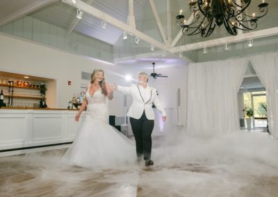 Two brides sharing a first dance amid low fog in the white ballroom