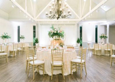 Reception hall with ivory linens, gold chairs and greenery centerpieces under an iron chandelier