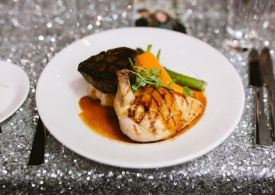 Plated entree of grilled chicken and beef medallion with vegetables