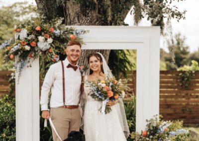 Bride and groom with their dog at a citrus-and-floral ceremony backdrop under a live oak
