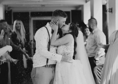 Bride and groom share a kiss during a lively confetti send-off as guests cheer