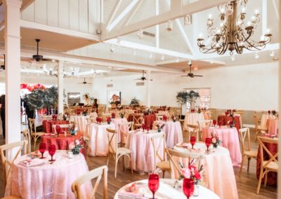 Vaulted reception hall with pink and red linen tables under a chandelier