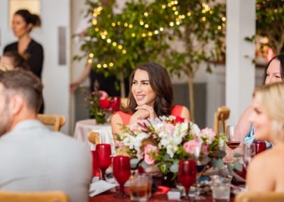 Guest in red smiling at a reception table set with red goblets and floral centerpieces