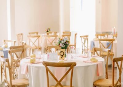 Round reception tables with cross-back wooden chairs and blush runners in a bright event hall