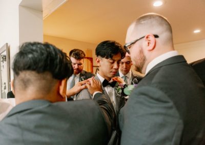 Groomsmen gathered close to help the groom with his bow tie before the ceremony