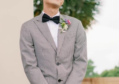 Smiling groom in a gingham blazer and bow tie with a wildflower boutonniere