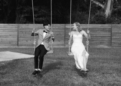Black-and-white of a bride and groom on side-by-side rope swings on the lawn