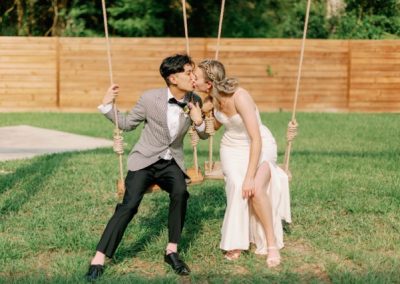 Bride and groom kissing while seated on rope swings on the lawn