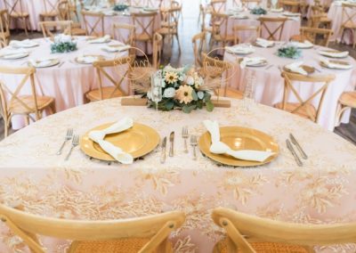 Sweetheart table with gold chargers and a sunflower centerpiece on patterned blush linen