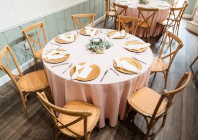 Round table with blush linen, gold chargers and a greenery centerpiece